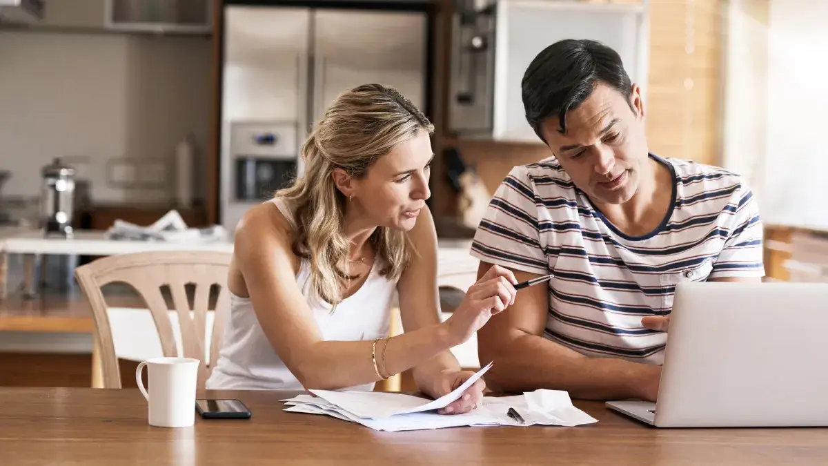 Man and woman sitting at the desk, talking, looking at the laptop screen