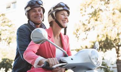 Smiling couple riding a scooter together, both wearing helmets and looking ahead