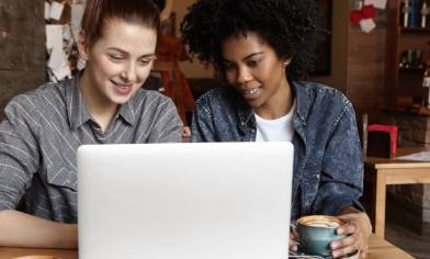 Two female students working on common university project using laptop computer together at cafe 