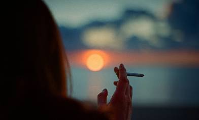 A person smoking a cigarette at sunset