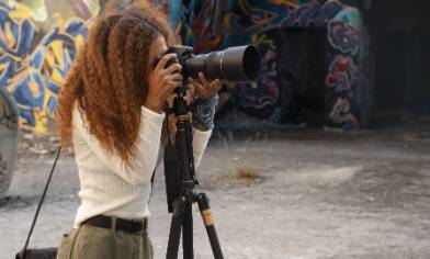 A person operating a camera mounted on a tripod in a location with graffiti walls