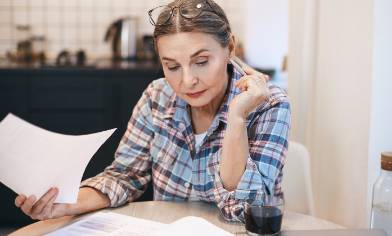 A person sitting at a table reading a document, pen in hand