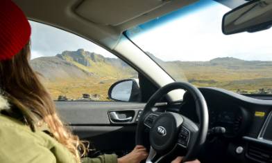 a person with long hair and a red beanie hat looking out at a mountainous landscape from behind the wheel of a car