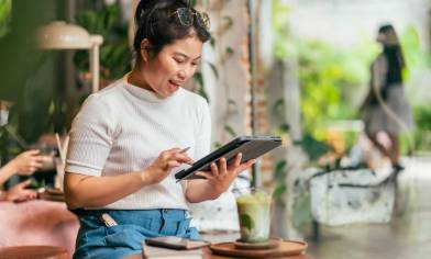 Smiling person using a tablet at a cafe table, with an iced coffee and tablet device 