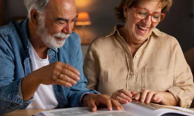 Two people sit at a table under warm lighting, looking through a photo album 