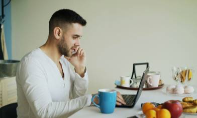 A person sitting at a table on the phone with a laptop and blue mug