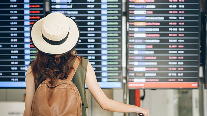 Woman wearing hat and backpack at airport looking a departure board at the airport