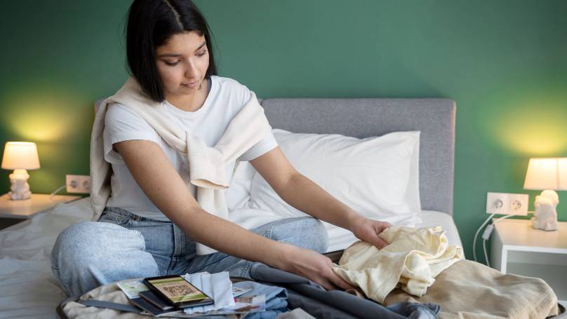 a person sitting on a bed packing a suitcase