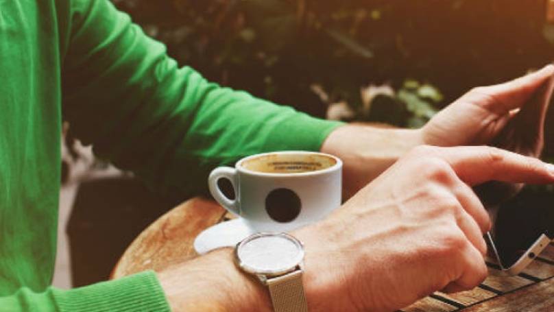 a person in a green jumper browsing a tablet and having coffee