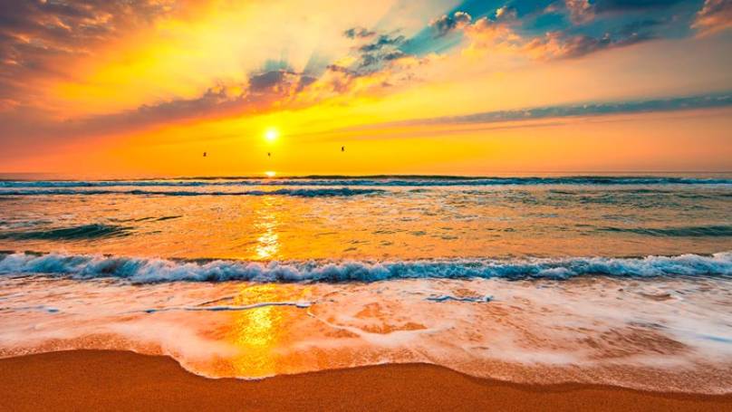 Beach with sea waves lapping on to beach and a beautiful sunset in the distance