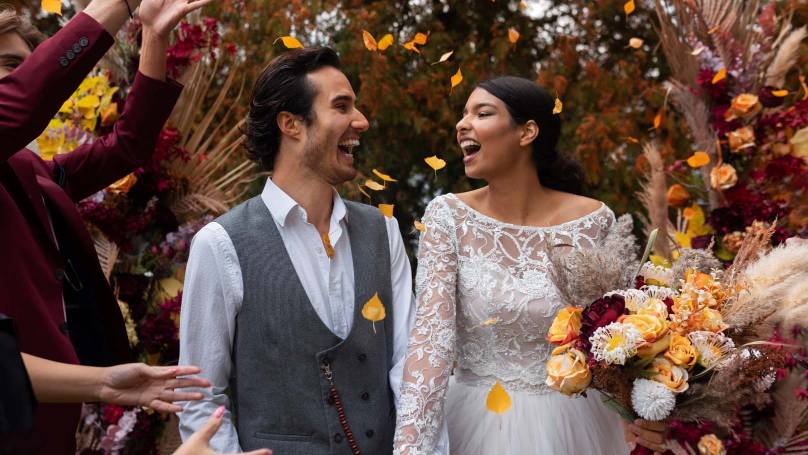 a newly married couple broadly smiling as their guests shower them with flower petals