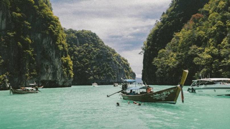 Lagoon with boats surrounded by rocky green hillside in Thailand