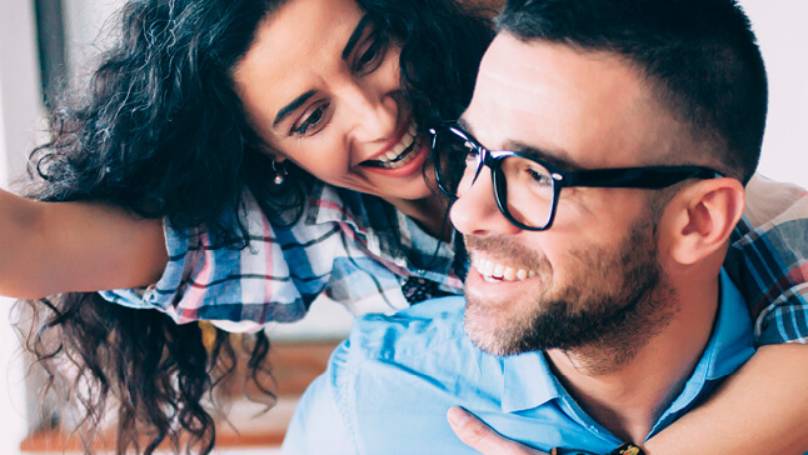 Young couple in kitchen both smiling while woman holds dangling key out in front of man