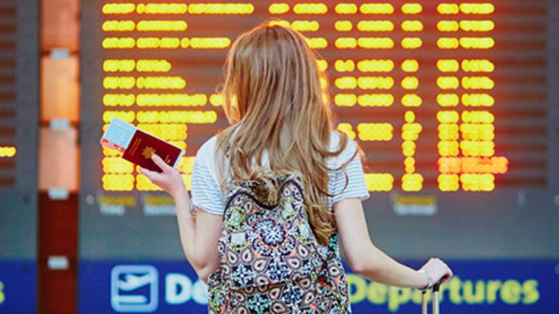 young lady checking the flight times on the board whilst holding her passport