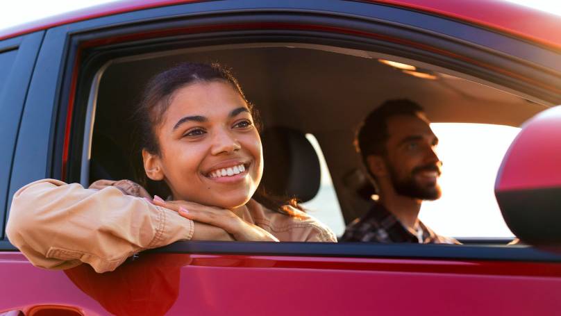 a person driving and a person looking out of the window of a red car