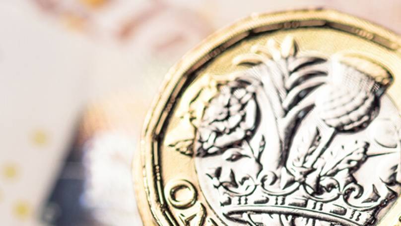 A £5 bank note placed on the left, a British one pound coin, face up on the right