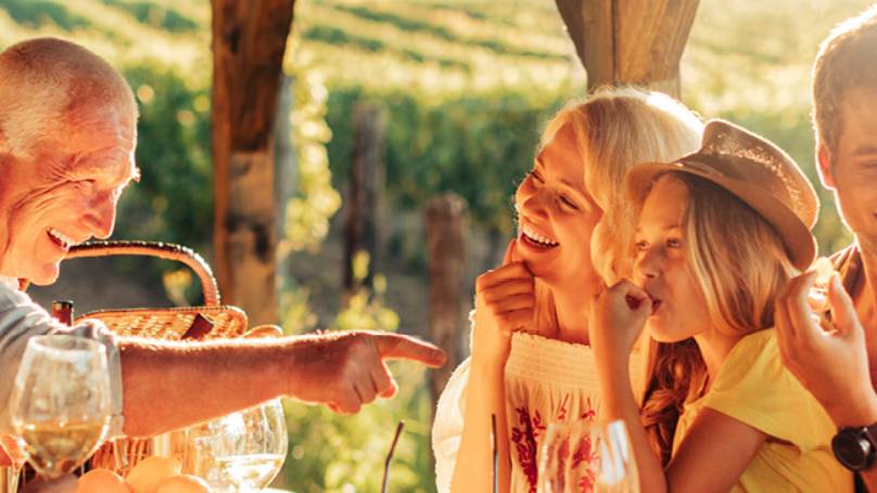 Sunlit family picnic, grandparents making fun gesture at grandchildren, parents looking on lovingly