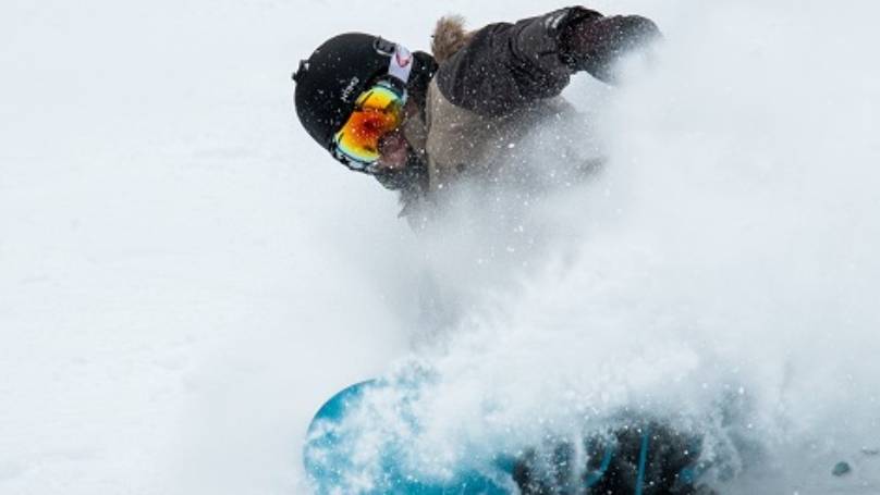 Person snowboarding through snow surrounded with snow spray