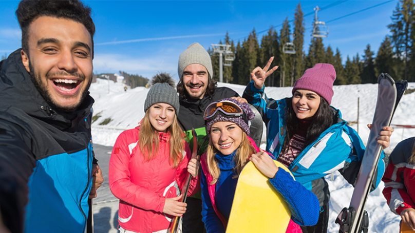 young men and women friends with skiing equipment take selfie