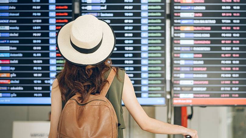 Woman wearing hat and backpack at airport looking a departure board at the airport