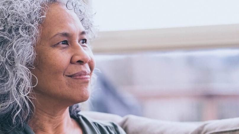 Mature woman sat on a couch, smiling as she looks out of the nearby window