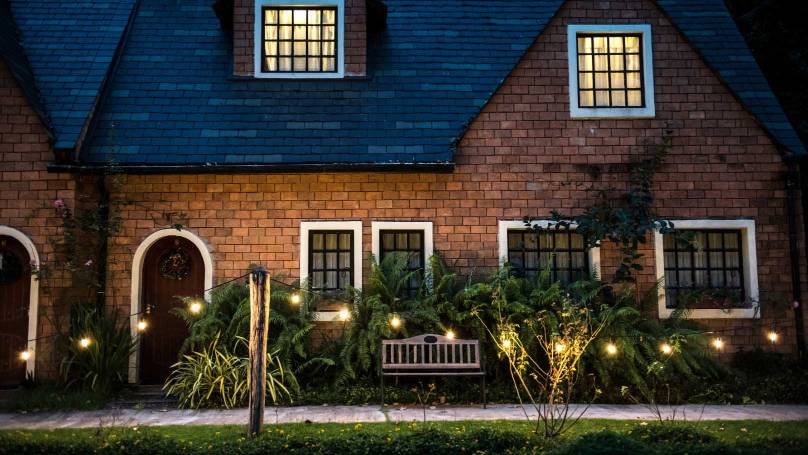 two storey pitched roof house at night with light in the upper windows and in the garden