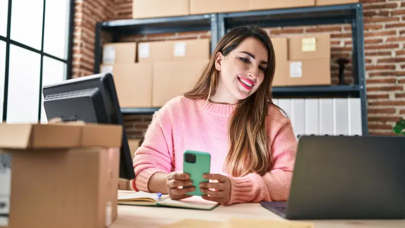 a smiling person surrounded by parcels with a smartphone and laptop 
