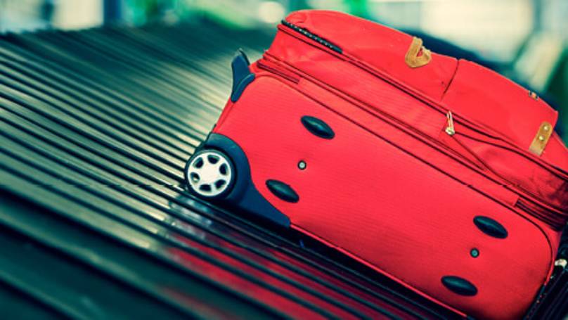 Red suitcase on airport conveyor belt at luggage reclaim