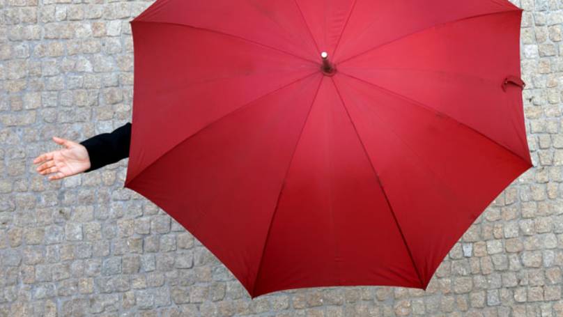 Person on cobble street under an open red umbrella holding their hand out to feel the rain