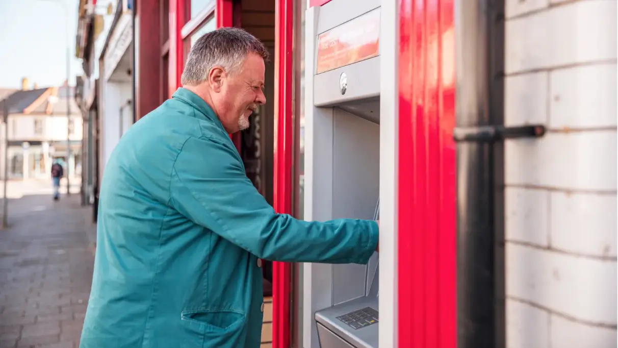 Side view of a man standing at a Post Office branded cash machine outside a branch on a high street