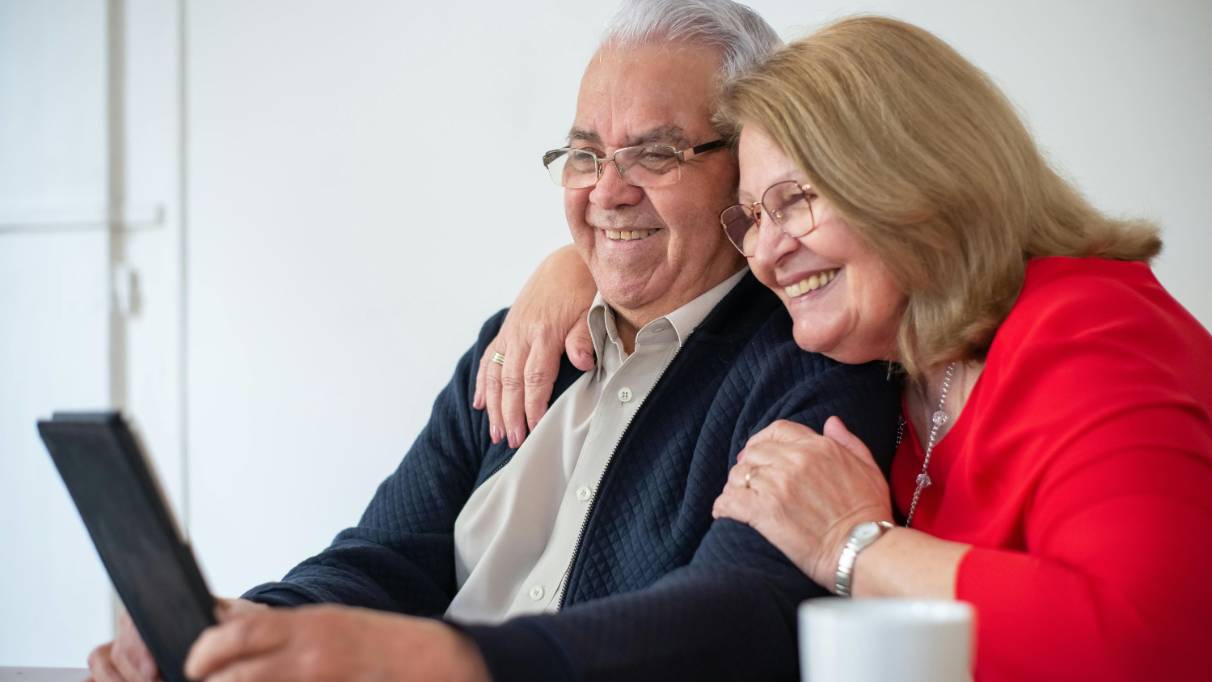 Elderly couple smiling while looking at an electronic tablet