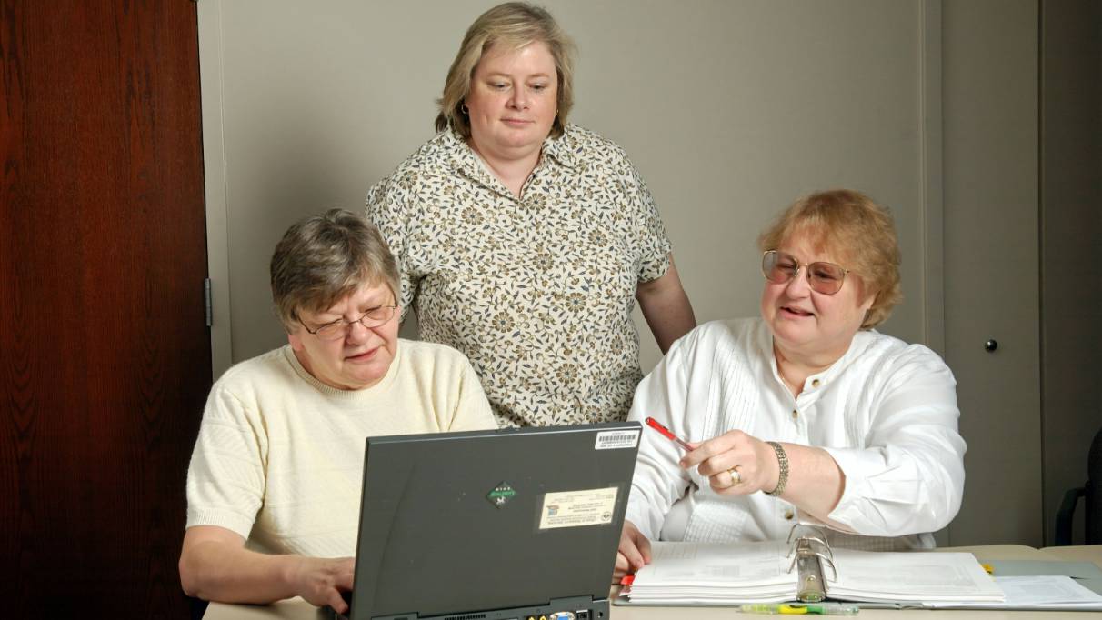 Three adults reviewing a binder of papers in front of an open laptop