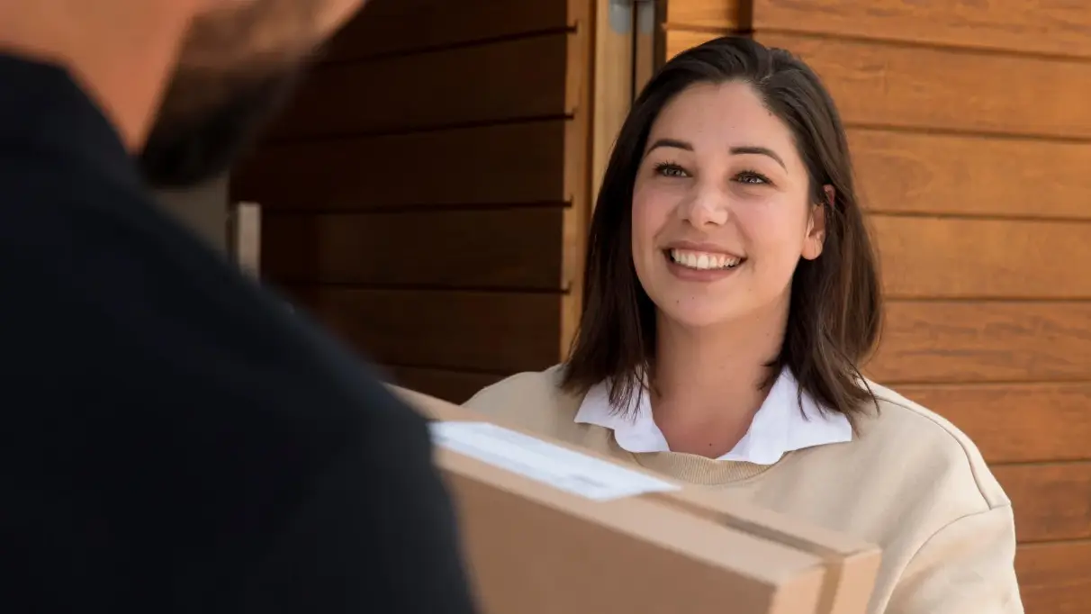 A delivery person hands a package to a smiling homeowner outside an open front door.