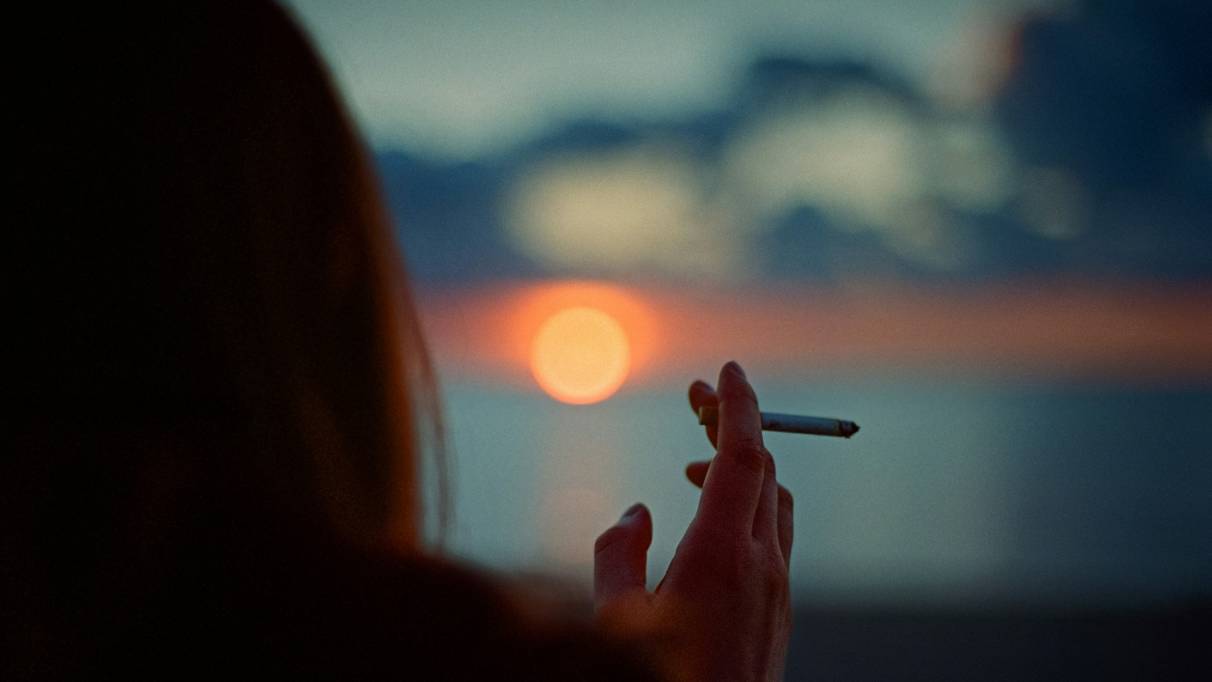 A person smoking a cigarette at sunset