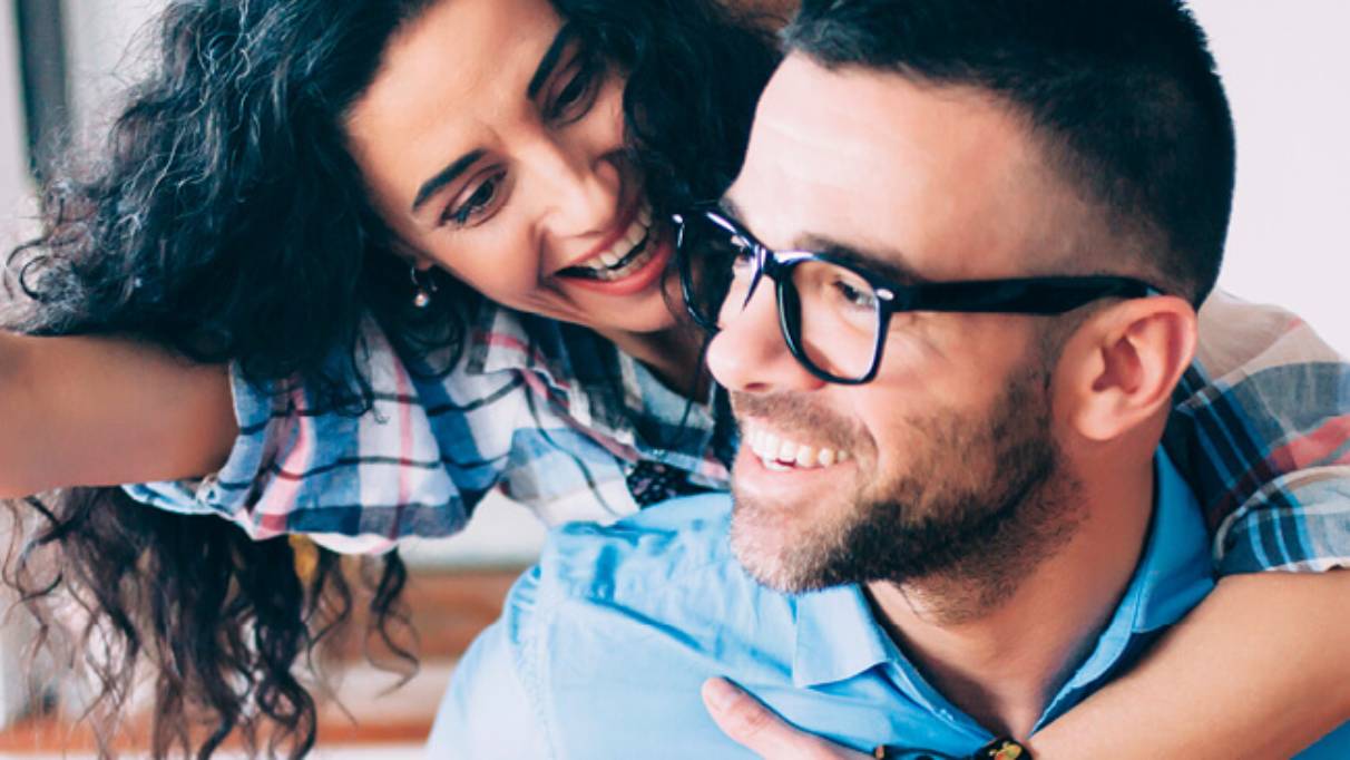 Young couple in kitchen both smiling while woman holds dangling key out in front of man