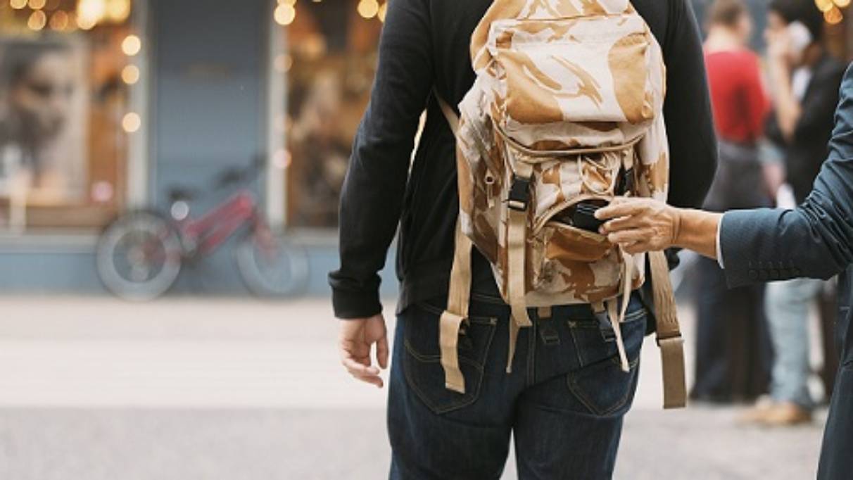 Man with rolled sleeve taking item from backpack on another man walking in ahead in a street
