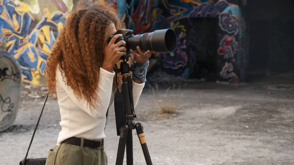 A person operating a camera mounted on a tripod in a location with graffiti walls