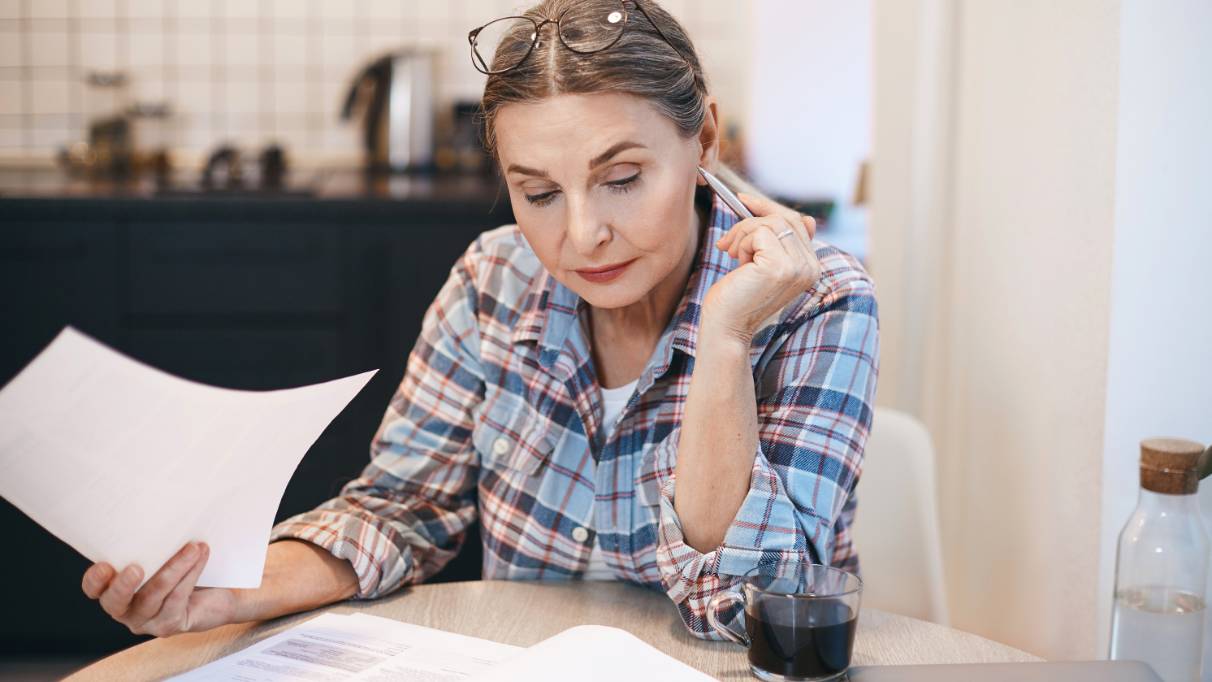 A person sitting at a table reading a document, pen in hand