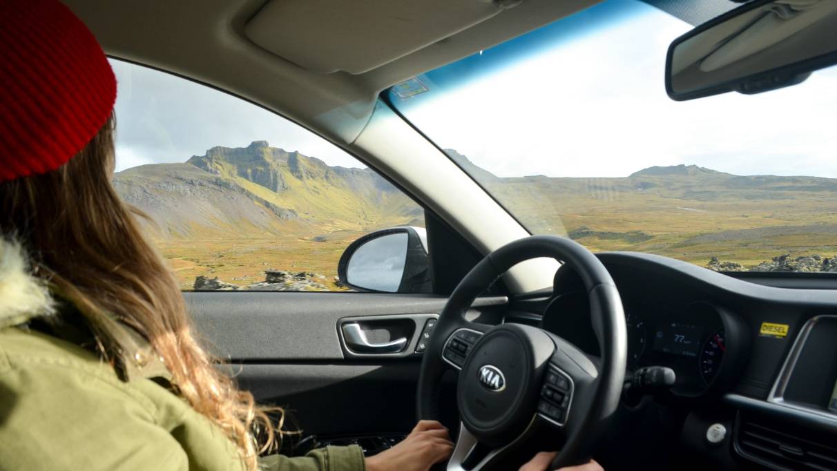 a person with long hair and a red beanie hat looking out at a mountainous landscape from behind the wheel of a car