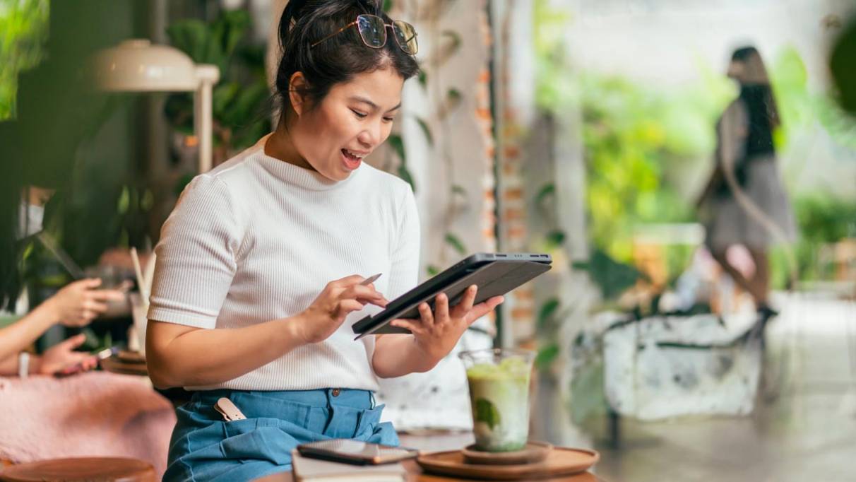 Smiling person using a tablet at a cafe table, with an iced coffee and tablet device 