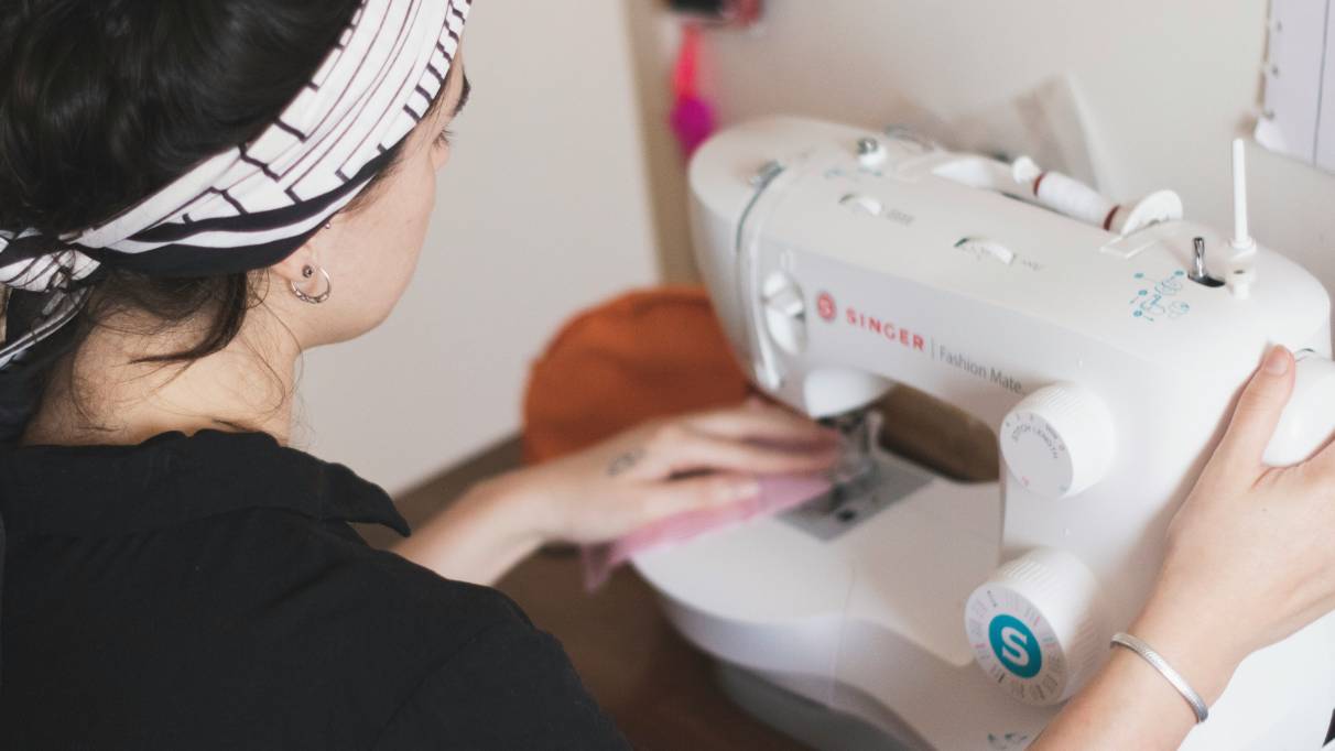 A person operating a white Singer sewing machine while stitching a piece of pink fabric.