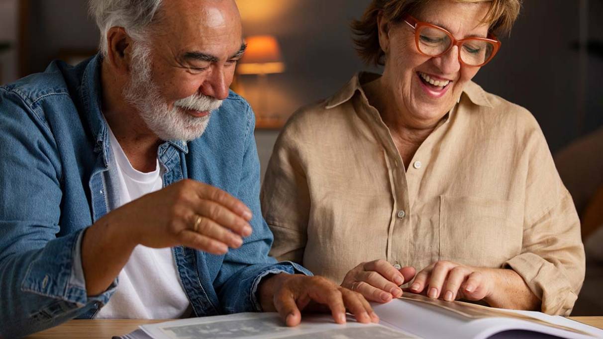 Two people sit at a table under warm lighting, looking through a photo album