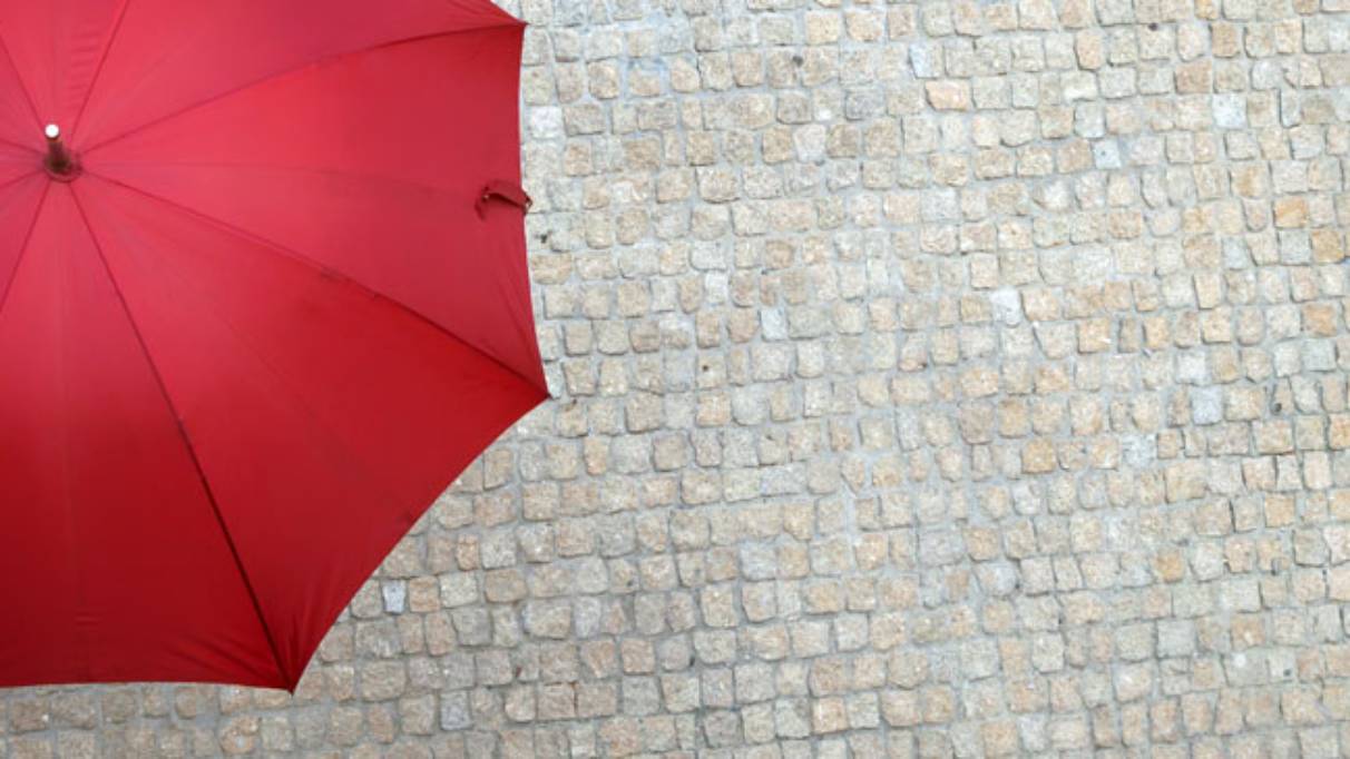 Person on cobble street under an open red umbrella holding their hand out to feel the rain