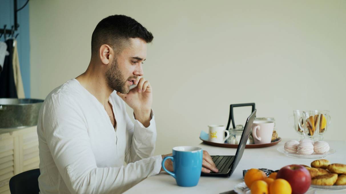A person sitting at a table on the phone with a laptop and blue mug