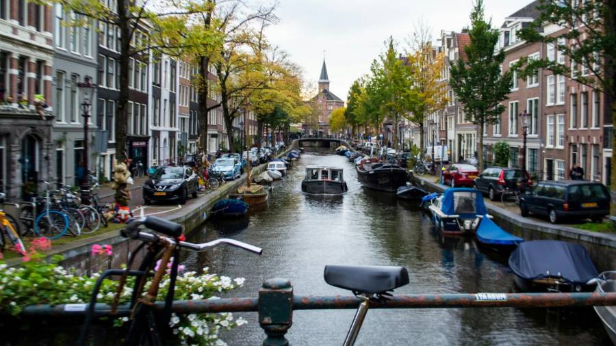 Canal in Amsterdam lined with houses, boats and bicycles on a bridge