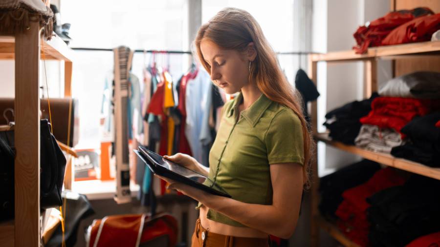 Someone’s in a room full of clothes and accessories, using a tablet while surrounded by shelves and racks of fashion gear