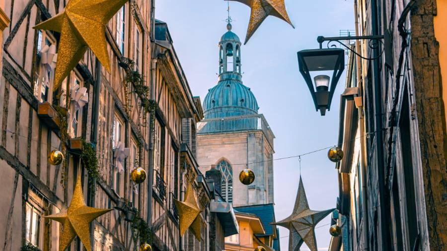 Narrow street with timber-framed buildings decorated with golden stars and a church dome in the background