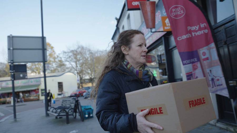 A person carrying a cardboard box marked 'FRAGILE' outside a Post Office branch