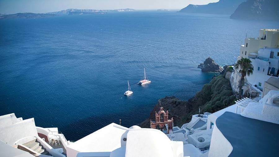 White buildings overlook a blue sea with sailboats and distant islands