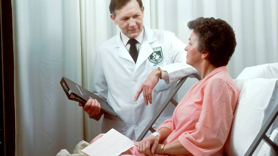 Doctor speaking to patient at her bedside. Patient wearing a salmon-coloured gown